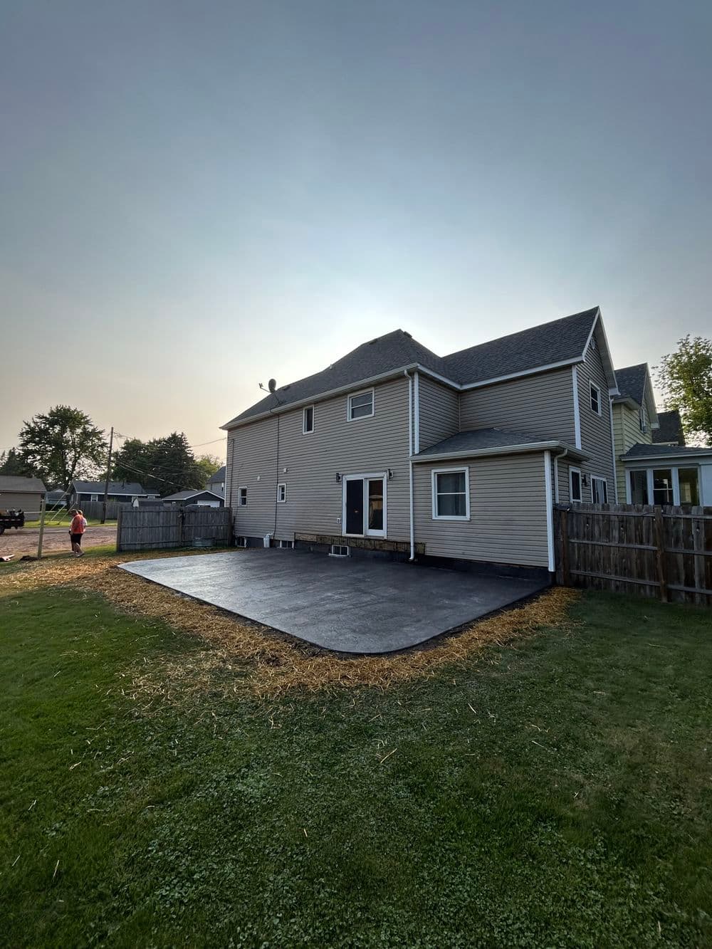 Newly paved backyard patio beside a two-story house with clear blue sky.