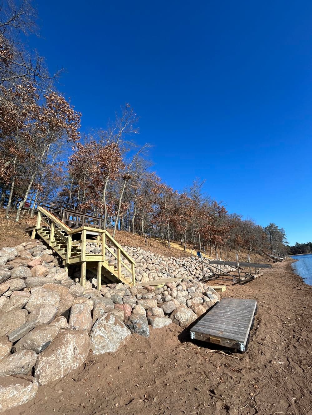 Wooden stairs lead to a lakeshore with rocky scenery under a clear blue sky in autumn.