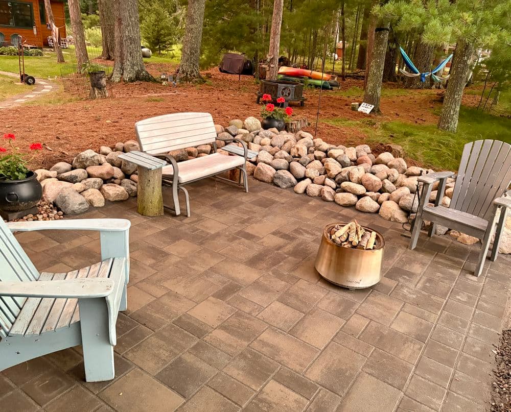 Cozy outdoor patio with stone seating area, fire pit, and lush greenery in background.