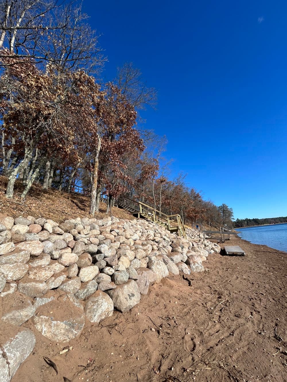 Rocky shoreline with trees and clear blue sky at a serene lakeside location.
