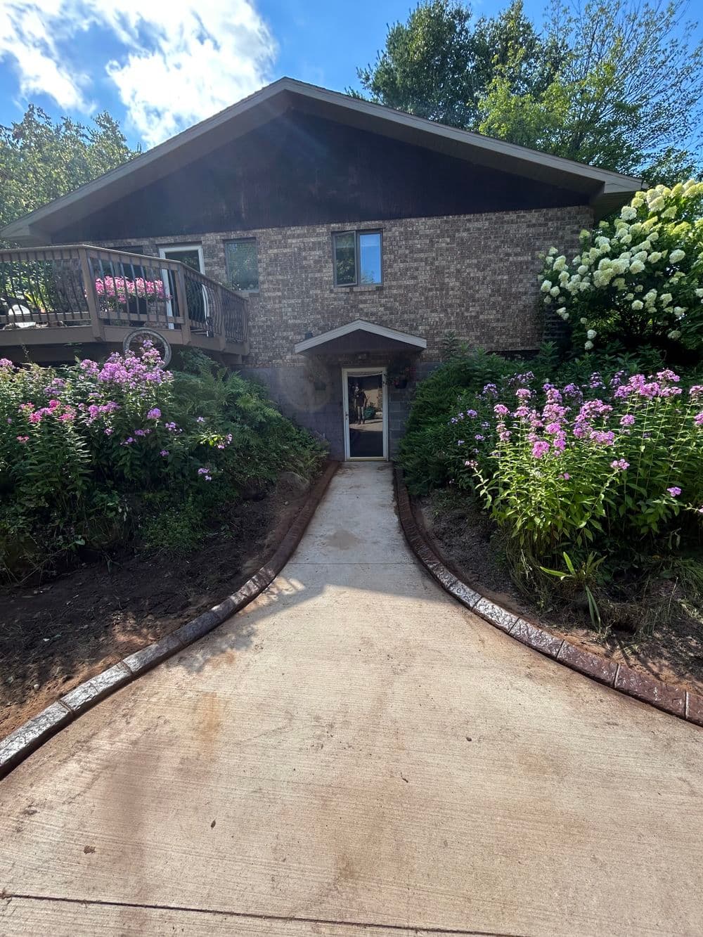 Charming brick house with landscaped garden and pink flowers in front, under a blue sky.