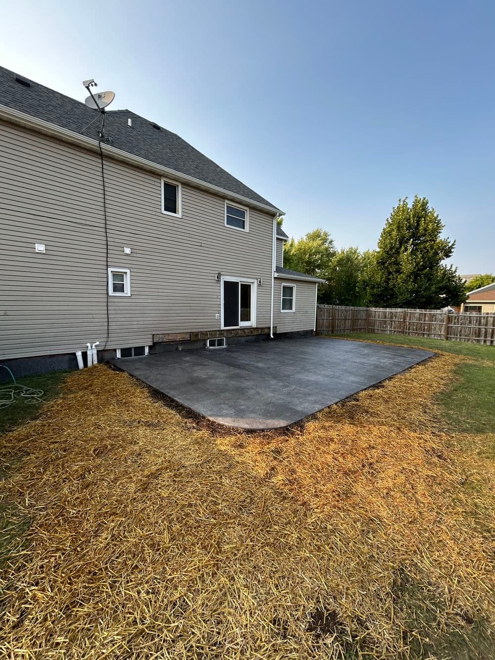 Backyard renovation featuring a new concrete patio and straw-covered landscaping.