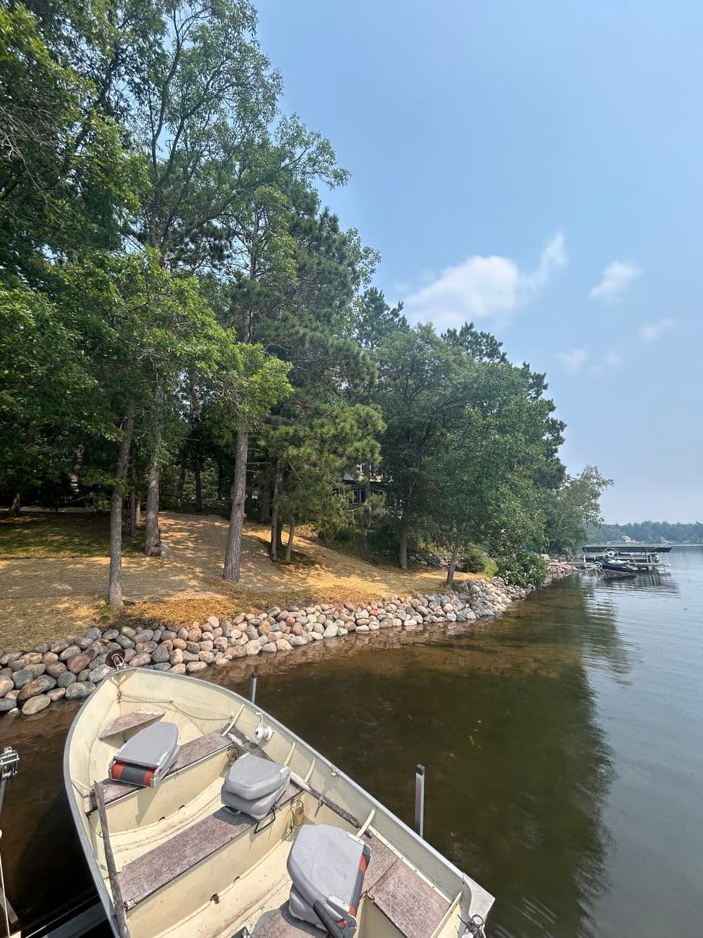 View of a peaceful lake with a boat docked, surrounded by trees and rocky shoreline.